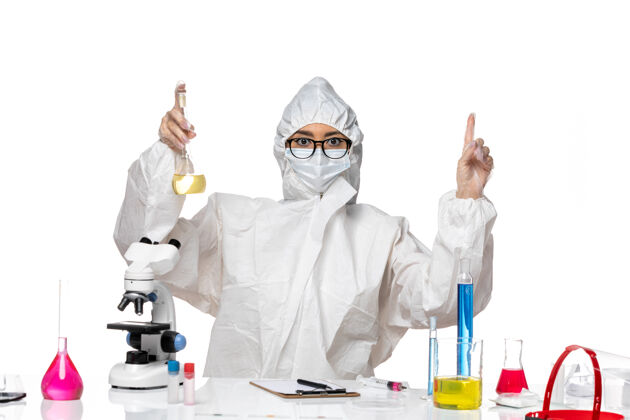 专业正面图身穿特殊防护服的年轻女化学家在白桌子上拿着烧瓶实验室病毒化学病毒医学化学
