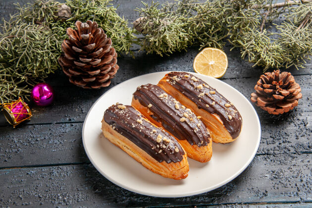 盘子下图：白色椭圆形圆锥形板上的巧克力蛋糕 冷杉树叶 圣诞玩具 黑色木制背景上的柠檬片锥午餐黑暗