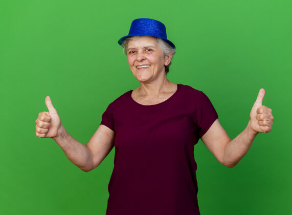 老人微笑着戴着派对帽的老太太竖起大拇指 两手看着绿色的相机拇指女人帽子