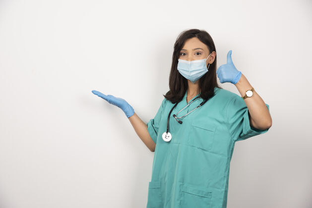 制服戴着医用面罩和手套的年轻医生在白色背景上竖起大拇指高质量照片医疗职业手套