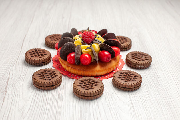 水果下面是红色椭圆形蕾丝doily上的浆果蛋糕和白色木桌上的饼干蕾丝烘焙甜点