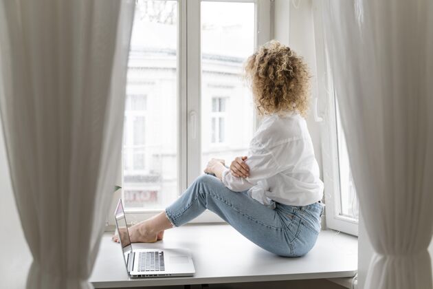 笔记本电脑金发卷发女人在家靠窗休息室内活动宁静休闲