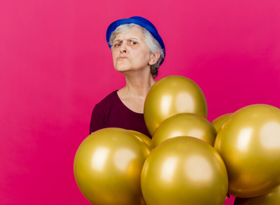 帽子笨手笨脚的老妇人戴着聚会帽站在粉红色的气球上气球女人站着