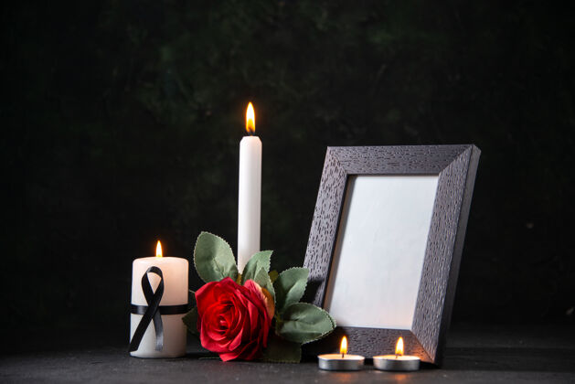 死亡正面图：带相框的白色蜡烛和深色桌子上的花朵葬礼邪恶的死亡图画蜡烛烛光