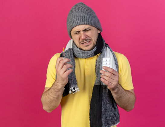 注射器年轻的金发病斯拉夫男子戴着冬季帽子和围巾拿着注射器男人药丸围巾