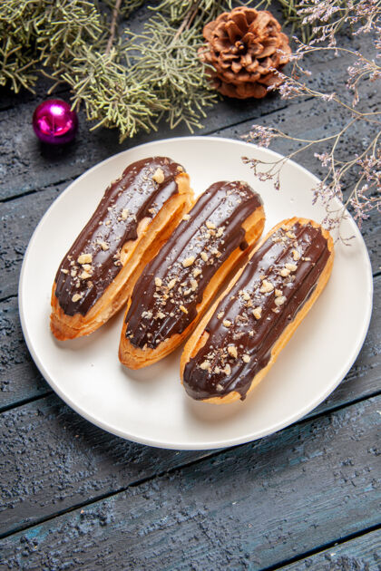 底部底视图巧克力eclairs在白色椭圆形板冷杉树枝锥形圣诞玩具在黑色木桌上三明治美味晚餐