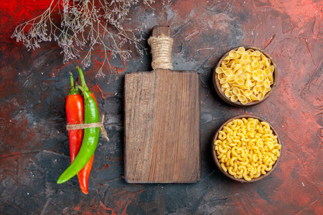 扎不同颜色和大小的生面团辣椒的俯视图 用绳子和木制砧板在混合色背景上相互捆扎在一起食物另一个蔬菜