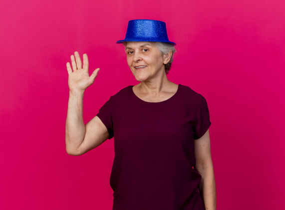手微笑着戴着聚会帽的老妇人站在那里 举手站在粉红色的椅子上站起来聚会女人