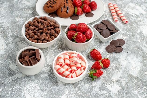 食物底视图饼干草莓和圆形巧克力放在白色椭圆形盘子碗里 糖果草莓巧克力麦片放在灰白色的地面上椭圆形可食用水果巧克力