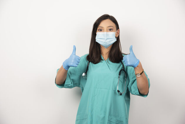 妇女戴面具的女医生在白色背景上竖起大拇指高质量照片医生保健手套