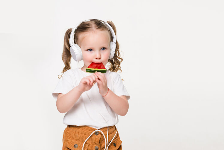 孩子戴着耳机吃糖果的小女孩的画像耳机美丽糖果