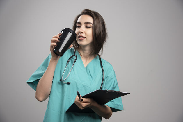 职业年轻的医生喝咖啡在灰色背景高品质的照片女性疾病工作