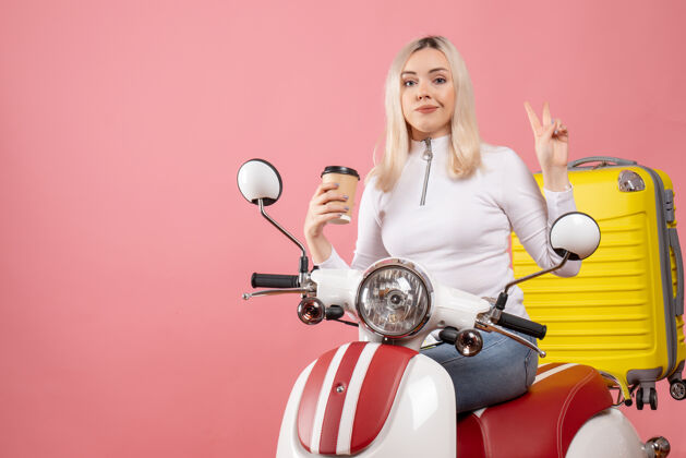 前面前视图骑着轻便摩托车的年轻女士拿着咖啡杯制作胜利标志汽车年轻女士咖啡