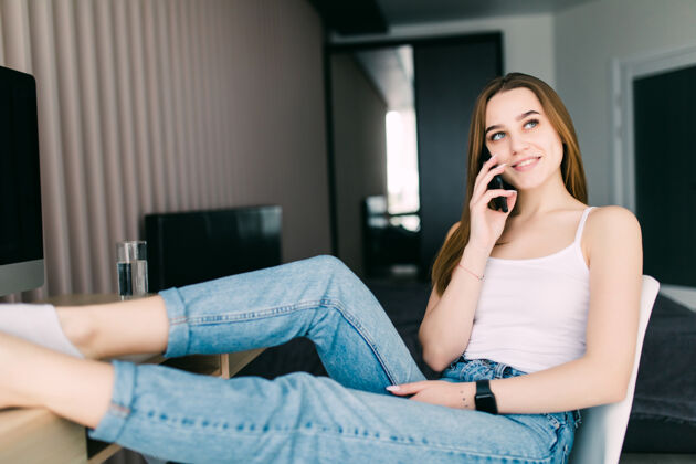 通讯坐在沙发上讲手机的快乐年轻女子坐着休闲公寓