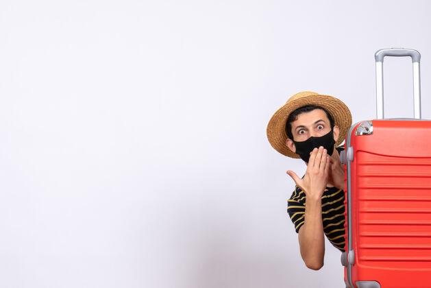 成人正面图是一个年轻的游客 黑色的面具藏在红色的手提箱后面人红色隐藏