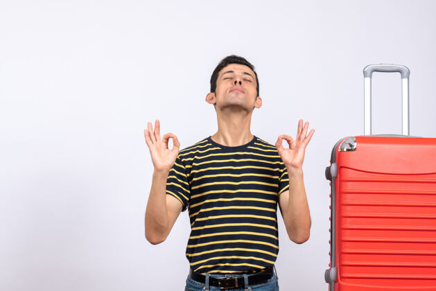 条纹正面图：一个穿着条纹t恤和红色手提箱的年轻人正在做一个“ok”的手势 闭上眼睛红色正面T恤