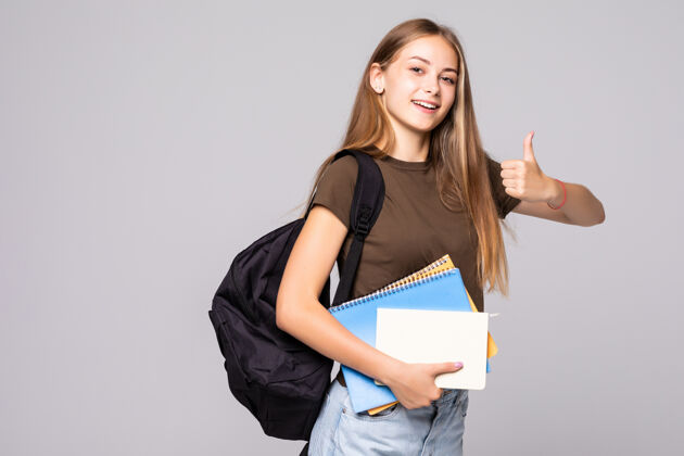 成功年轻的女学生拿着背包包 手拿大拇指向上的手势 隔着白墙拇指手势年轻