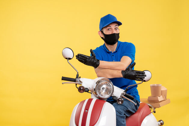 摩托车正面图黄色背景上身穿蓝色制服的年轻男性快递员柯维德-大流行快递服务工作病毒自行车工作送货蓝色传送带