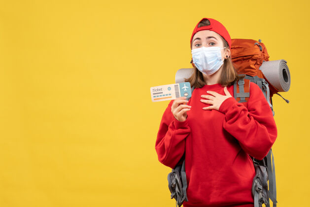 前面正面图：年轻的旅行女孩 背着背包 戴着面具 手放在胸前 手里拿着票票胸前面具