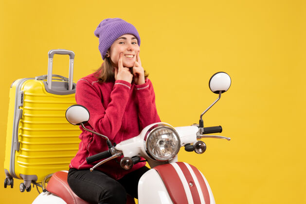 快乐前视图骑着轻便摩托车的年轻女子指着她的微笑年轻女子成人车辆