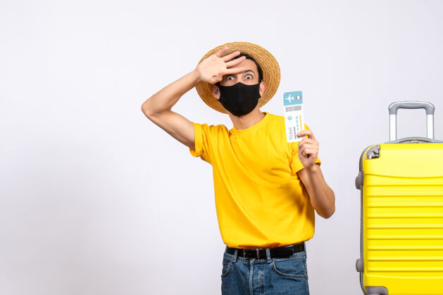 帽子正面图：拿着旅行票 戴着草帽的年轻人站在黄色手提箱旁视图站立手提箱