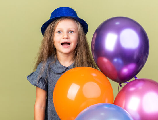 女孩兴奋的金发小女孩 戴着蓝色派对帽 手里拿着氦气球 被隔离在橄榄绿的墙上 还有复制空间生日氦气球
