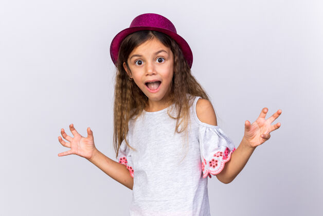 白种人惊讶的小白种女孩 戴着紫色派对帽 双手张开 在白色墙壁上与世隔绝 留着复制空间惊喜手帽子