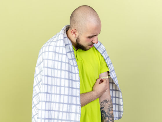 年轻年轻的病人裹着格子布 拿着隔离在橄榄绿墙上的温度计测量温度人表情包裹