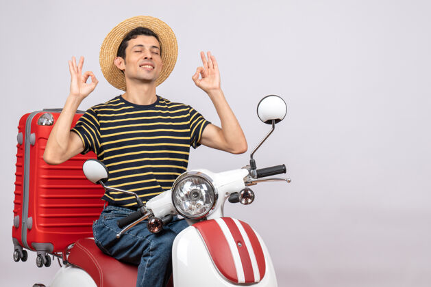 轻便摩托车一个戴着草帽的年轻人的前视图 他闭着眼睛做着“ok”的手势关闭帽子眼睛