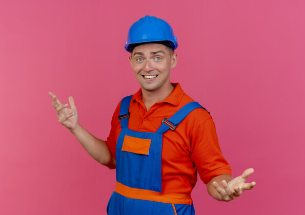 粉色微笑着的年轻男性建筑工人穿着制服和安全帽摊开双手传播背景安全