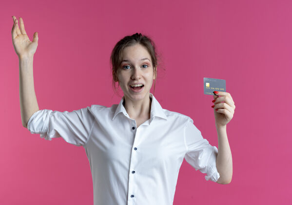 提高年轻惊讶的金发俄罗斯女孩拿着信用卡举手年轻惊喜粉红