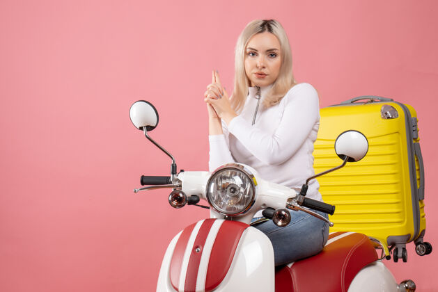车辆前视图年轻的金发女士骑着轻便摩托车做手指枪的标志坐着摩托车年轻的金发女郎