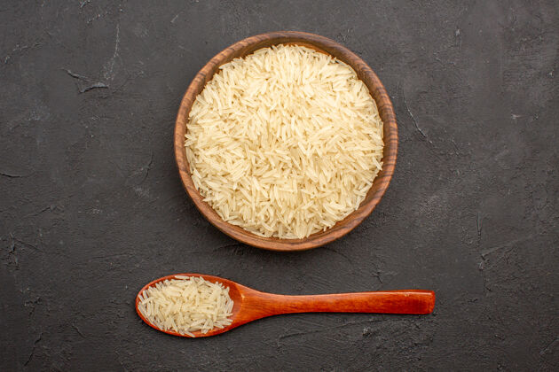 米饭灰色表面上棕色盘子里的生大米俯视图木勺食物炊具
