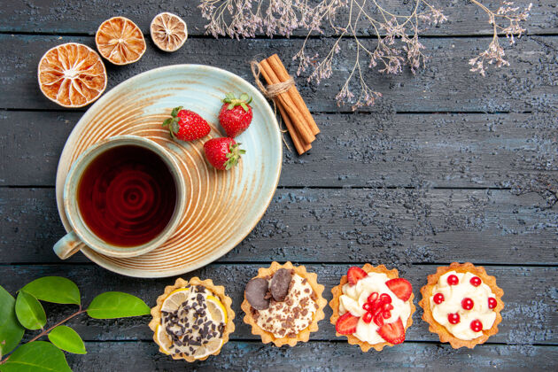 酸顶视图一杯茶和草莓放在茶碟上肉桂干橙子馅饼和叶子放在深色背景上食物小吃干