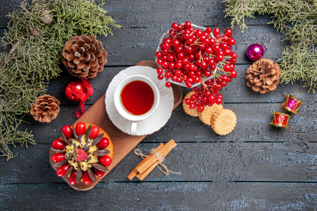 松果顶视图一杯茶和浆果蛋糕放在木制盘子里葡萄干放在玻璃松果里圣诞玩具冷杉树叶放在深色木制桌子上服务圣诞节桌子