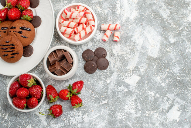碗白色椭圆形盘子上的饼干草莓和圆形巧克力灰白色桌子左上角的糖果草莓巧克力碗健康糖果盘子