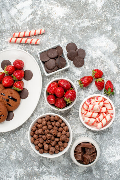 甜点顶视图饼干草莓和圆形巧克力放在白色椭圆形盘子碗里 糖果草莓巧克力麦片放在灰白色的桌子上可食用水果餐桌覆盆子