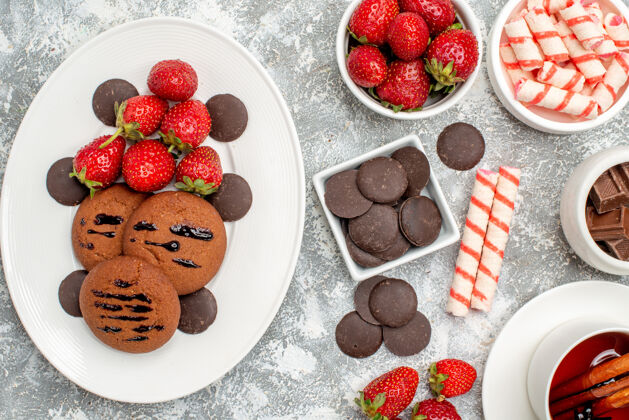 椭圆形顶近距离观察饼干草莓和圆形巧克力在椭圆形的盘子里草莓巧克力和肉桂茶在灰白色的桌子上新鲜浆果肉桂
