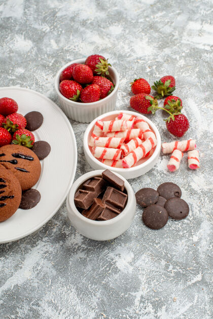 草莓上半部分查看饼干草莓和圆形巧克力在白色椭圆形盘子碗糖果草莓巧克力在灰白色的桌子上椭圆形一半盘子