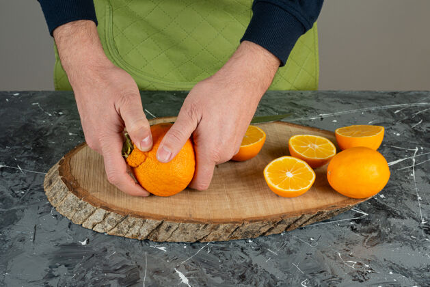 各种男人的手拿着多汁的橘子放在大理石桌上烹饪围裙有机