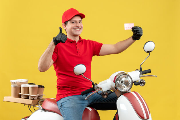 举行前视图的快递员身穿红色上衣 戴着帽子手套 戴着医用口罩 坐在摩托车上拿着银行卡 做着“ok”的手势车辆医疗面具