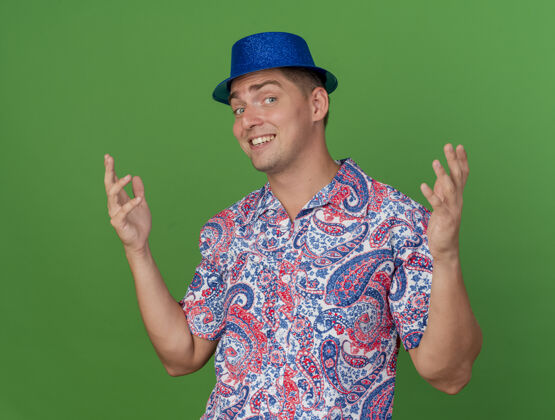 帽子戴着蓝帽子的年轻人微笑着 双手分开放在草地上穿蓝色绿色