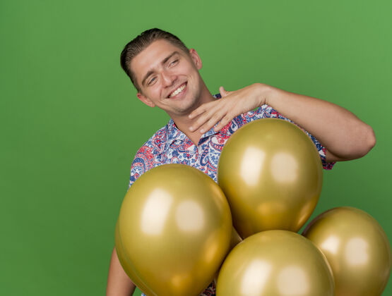小伙子面带微笑的年轻人穿着五颜六色的衬衫 站在绿色的气球后面站着气球年轻人