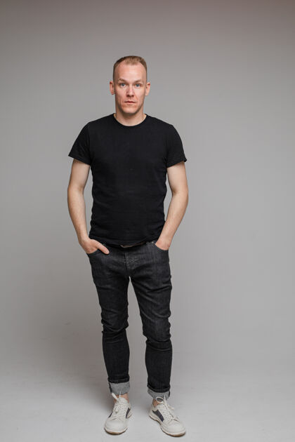 男性照片中 身着黑色t恤和牛仔裤的帅哥站在灰色墙上 双手插在口袋里英俊放松脸
