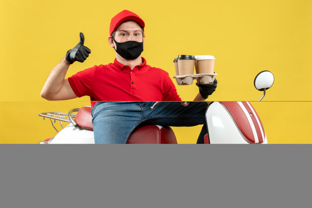 订单顶视图自信的送货员穿着制服 戴着帽子手套 戴着医用面罩 坐在滑板车上 竖起大拇指展示订单坐着摩托车摩托车