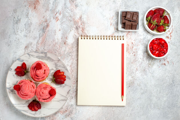 水果白色表面有果酱和巧克力棒的粉色草莓蛋糕俯视图饼干记事本容器
