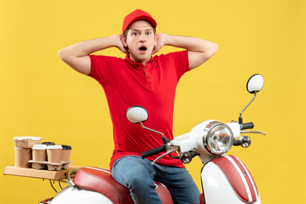 背景顶视图震惊的年轻人穿着红色衬衫和帽子传递秩序坐在黄色背景的踏板车上摩托车成人运动