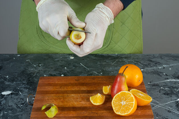 水果男人的手在大理石桌上切熟梨混合围裙橘子