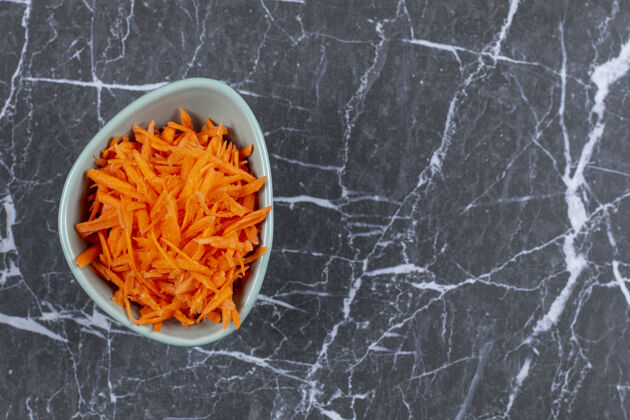 配料蓝色碗中新鲜磨碎的胡萝卜在黑色石头上的顶视图生的上菜胡萝卜
