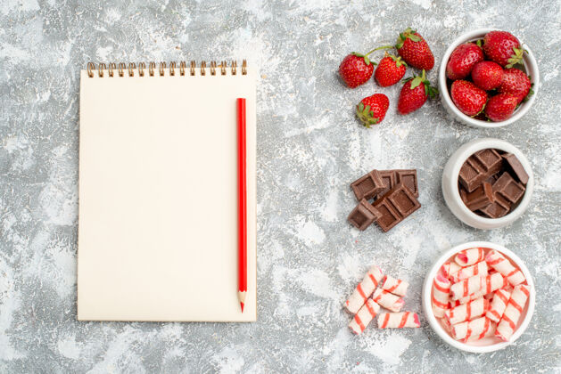 相框顶视图碗与草莓巧克力糖果和一些草莓巧克力糖果在右侧和笔记本与红铅笔在灰白的地面左侧左边笔记本草莓